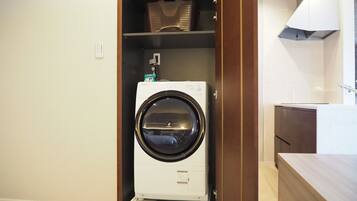 Une petite buanderie équipée d’un lave-linge à chargement frontal, d’une étagère au-dessus et d’un meuble en bois.