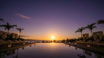 Una piscina infinita tranquila al atardecer, con sillones de descanso y palmeras.