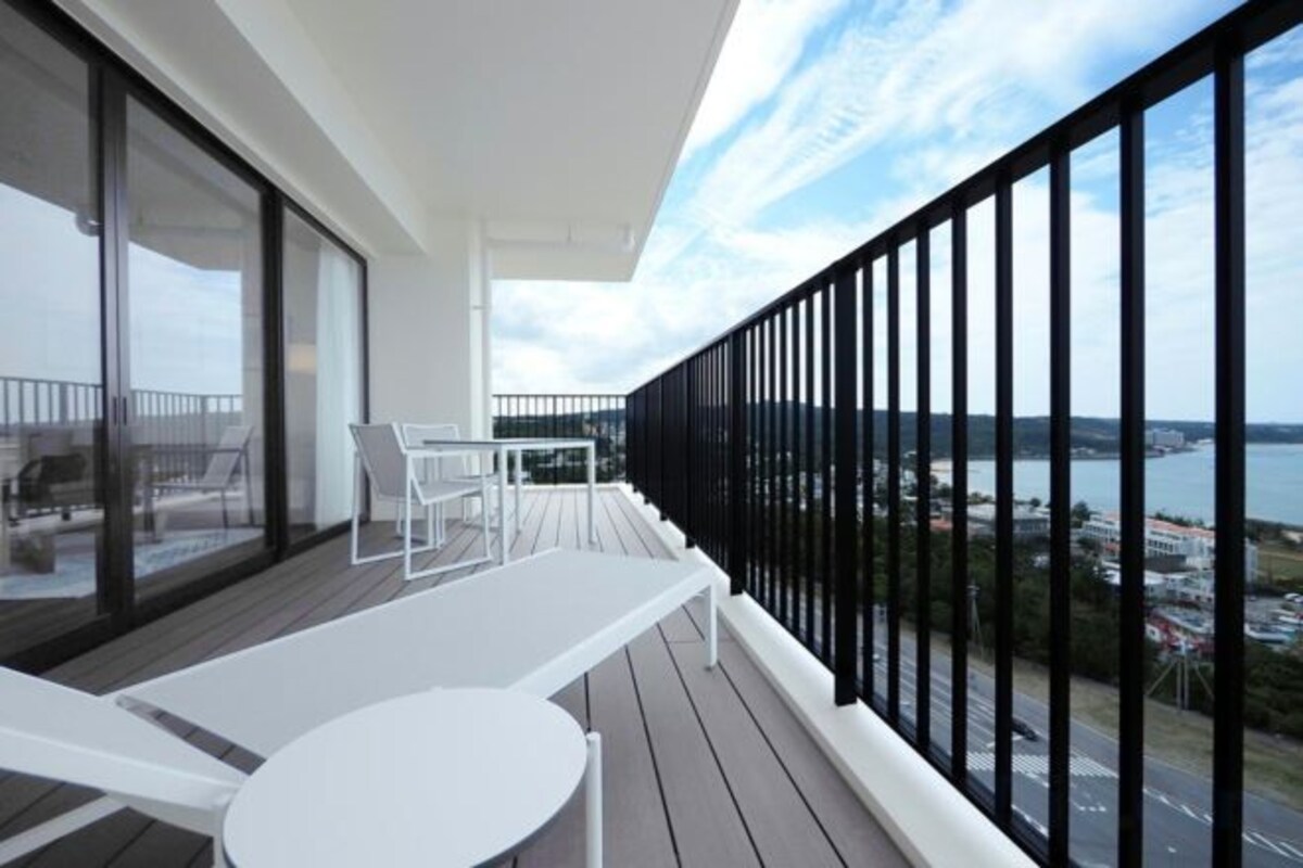 Un balcon avec une table et des chaises, une vue sur la mer et une rambarde noire.