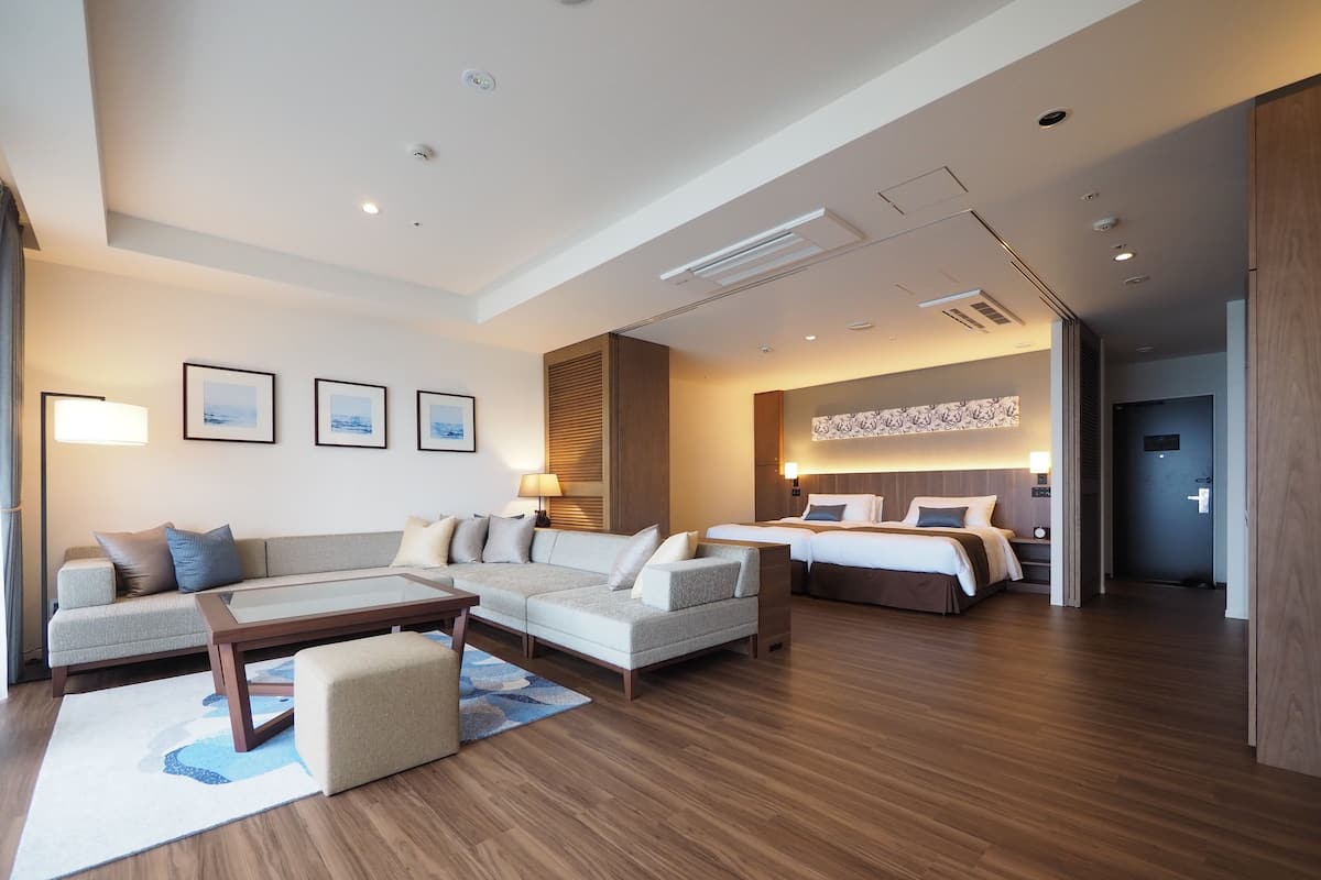 Une chambre d’hôtel moderne avec un canapé, deux lits, une table basse et une grande fenêtre.