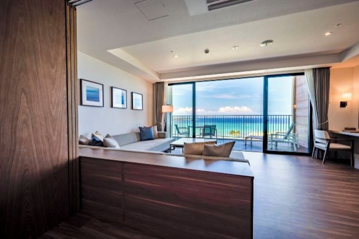 Une chambre d’hôtel moderne dotée d’un grand balcon, d’un coin salon et offrant une vue sur l’océan.