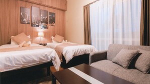 Habitación de hotel con dos camas, un sofá, una pared de madera decorada con cuadros, y un ventanal con cortinas.