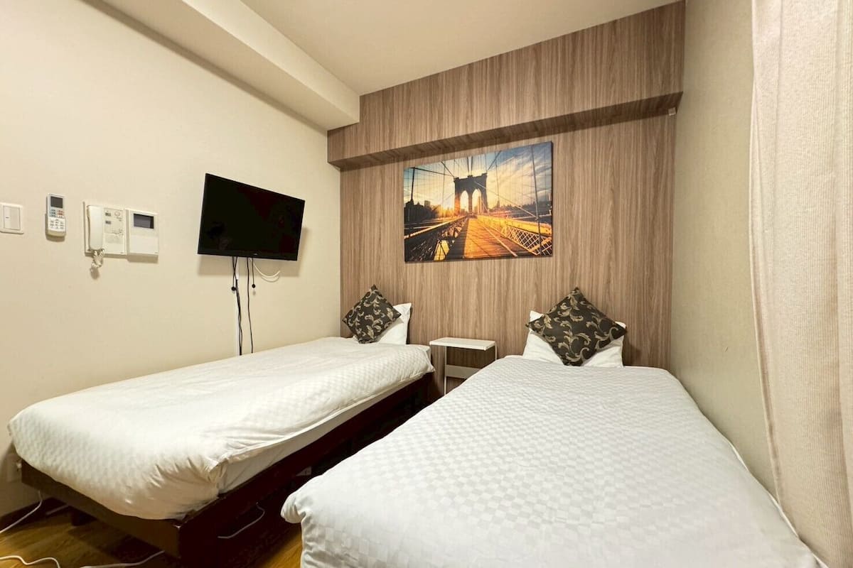 Een hotelkamer met twee eenpersoonsbedden, een aan de muur bevestigde televisie, een schilderij van een brug en een telefoon aan de muur.
