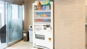 Una máquina expendedora con diversas bebidas y aperitivos, un cubo de basura y una puerta de vidrio.