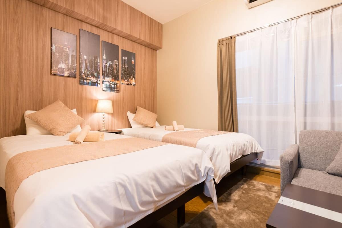 Een hotelkamer met twee bedden, een slaapbank, een stadsgezichtschilderij en een raam met gordijnen.