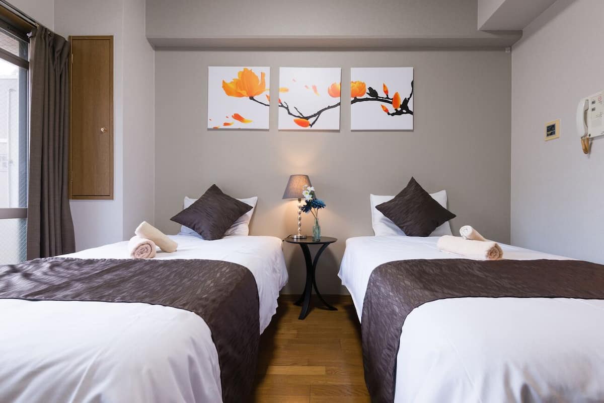 Een hotelkamer met twee bedden, een klein tafeltje met een lamp en drie aan de muur hangende schilderijen.
