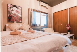 Une chambre avec un grand lit, une table de chevet, une chaise, une fenêtre avec des rideaux, un climatiseur fixé au mur et une affiche accrochée au mur.