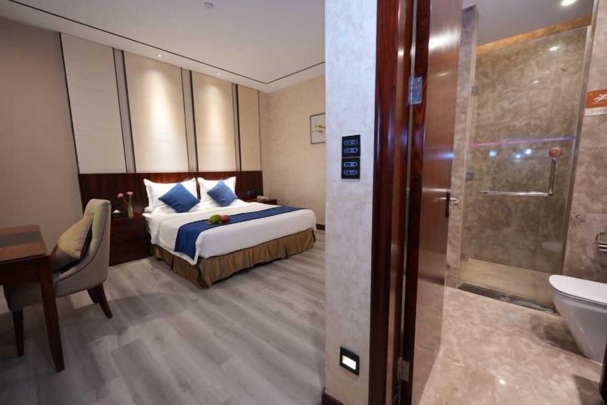 A hotel room with a bed, a desk, and a shower area.