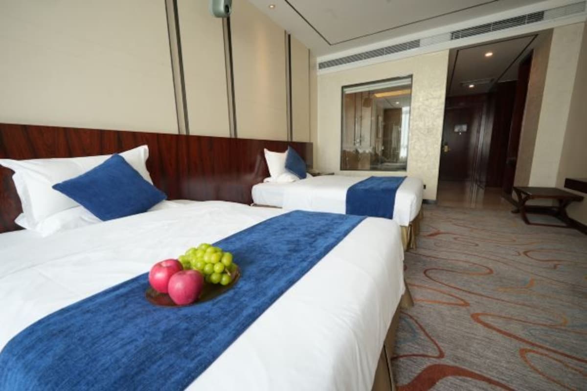 A hotel room with two beds, a blue bed runner, and a fruit arrangement on the bed.