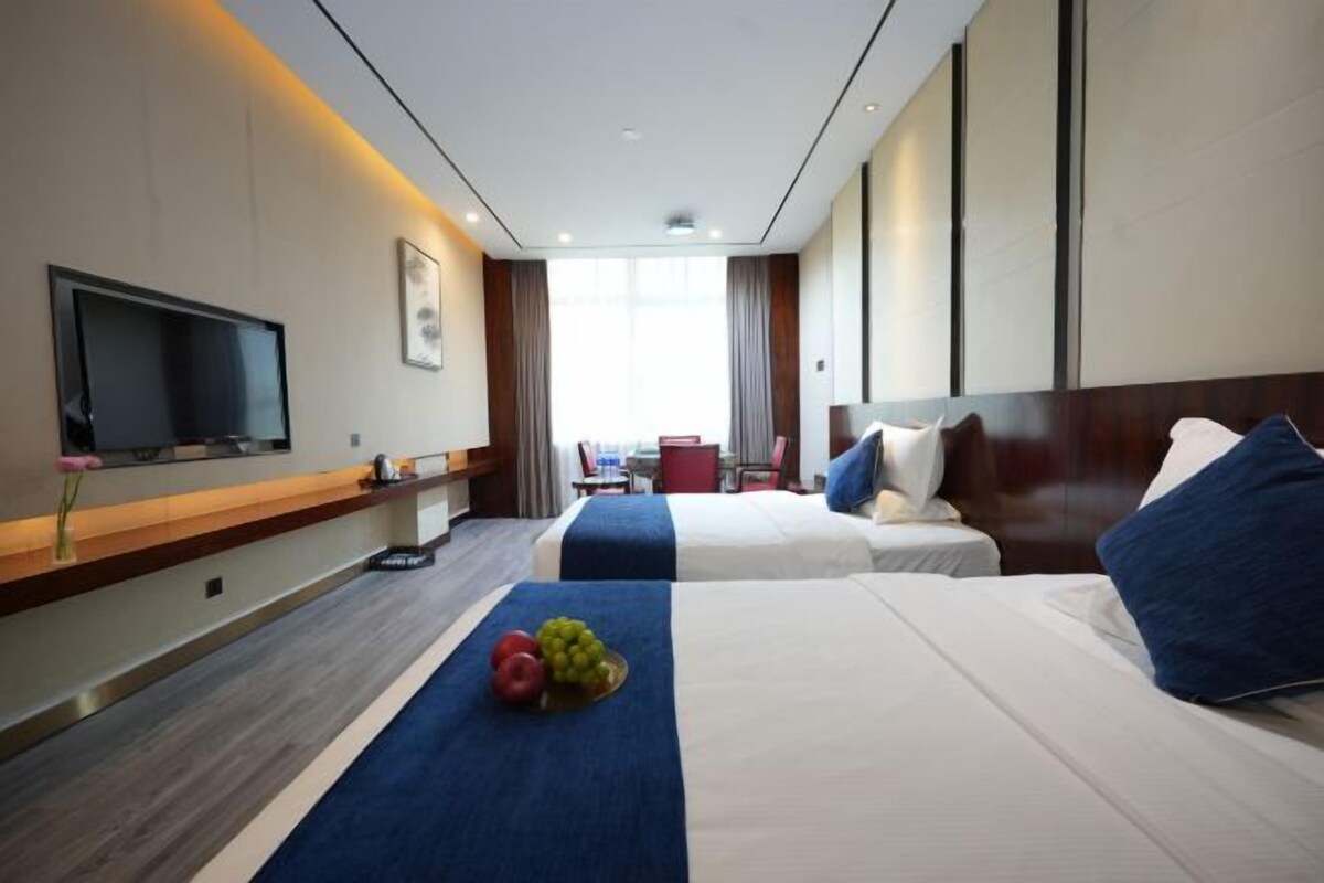 A hotel room with two beds, a flat-screen TV, a desk, and a window with curtains.