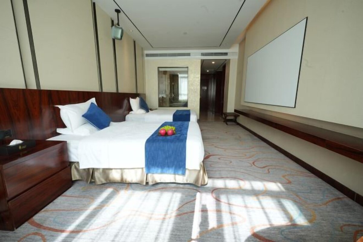 A hotel room with a large bed, a wooden nightstand, a desk, and a large window.