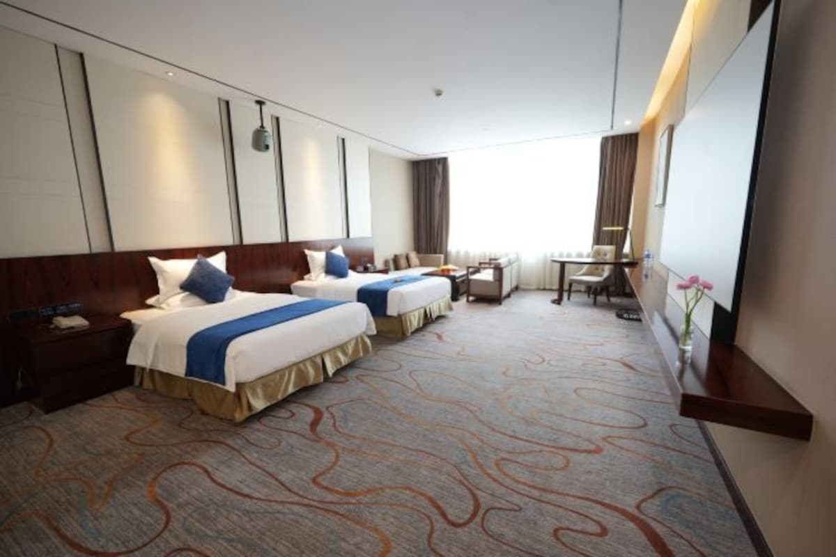 A hotel room with two beds, a desk, a chair, and a large window.