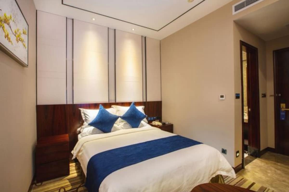 A hotel room with a large bed, a wooden headboard, a nightstand, and a painting on the wall.