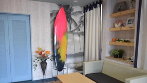Een kamer met een patroon vloer, een bank, een klein tafeltje, een surfplank, een muur met een palmboom muurschildering en een plank met decoratieve objecten.