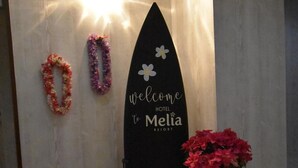 Een surfplank met daarop 'Welcome to Melia Resort', een klein tafeltje met een bloempot en twee bloemkransen aan de muur.