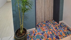 Een gang met een houten lift, een potplant en een kleurrijke mozaïektegelvloer.