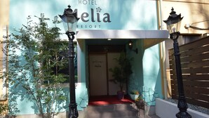 De ingang van Hotel Mella Resort met een rode loper, planten in potten en een bord dat gasten welkom heet.