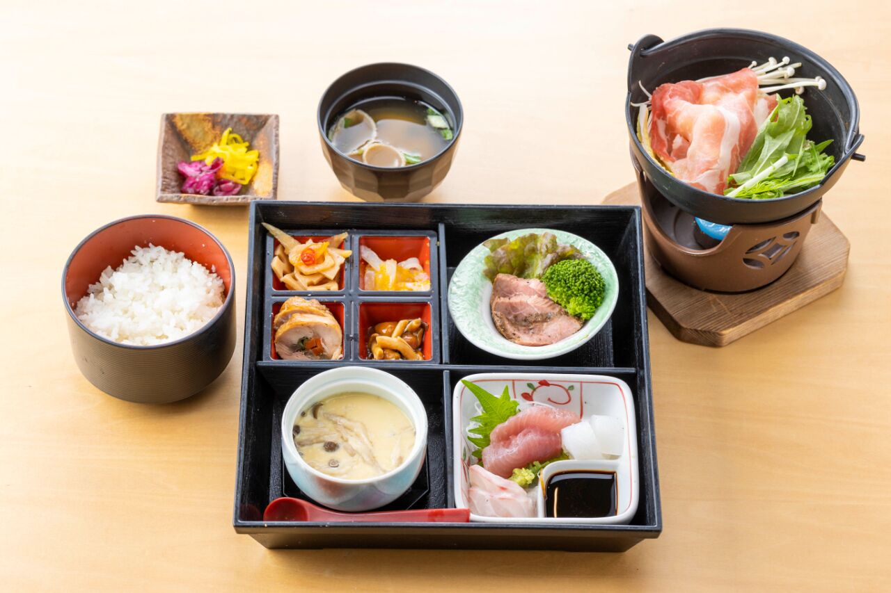 A traditional Japanese bento box with rice, fish, vegetables, and soup.