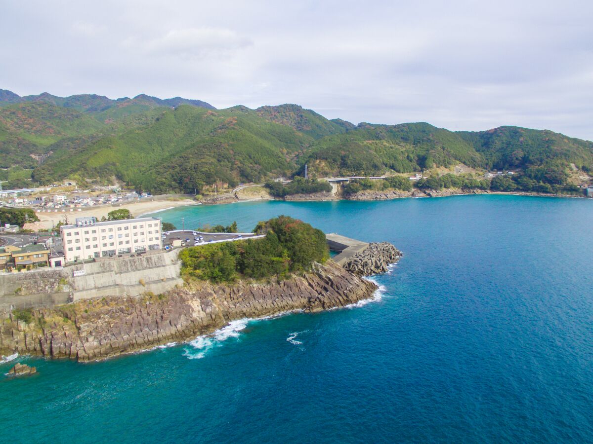Uma área costeira com um edifício grande, linha de costa rochosa e uma ponte ligando à terra firme.
