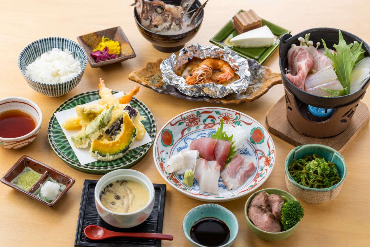 A variety of Japanese dishes including sushi, tempura, and a hot pot, arranged on a wooden table.