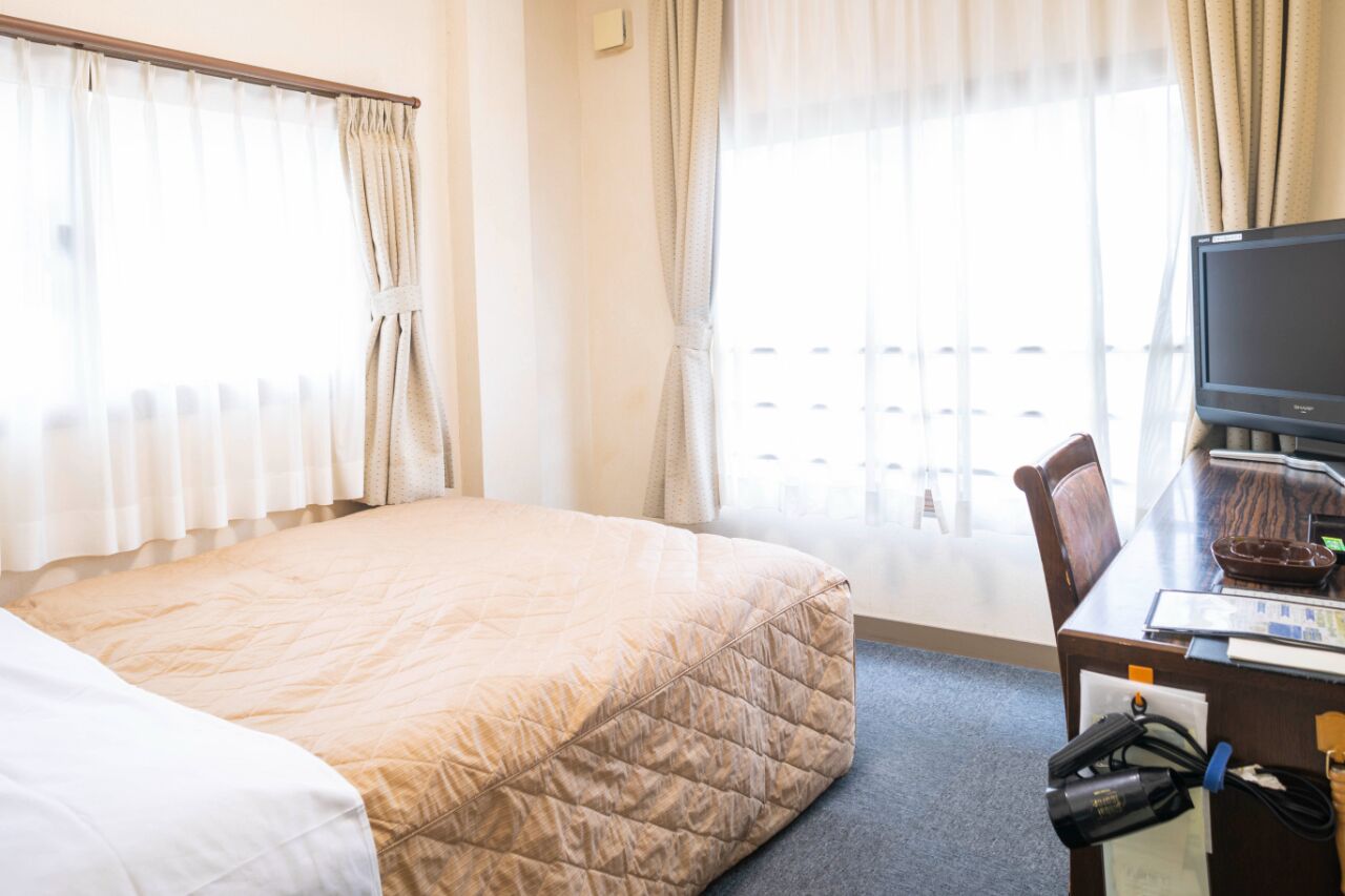 Una habitación de hotel con cama, escritorio con computadora y ventana con cortinas.