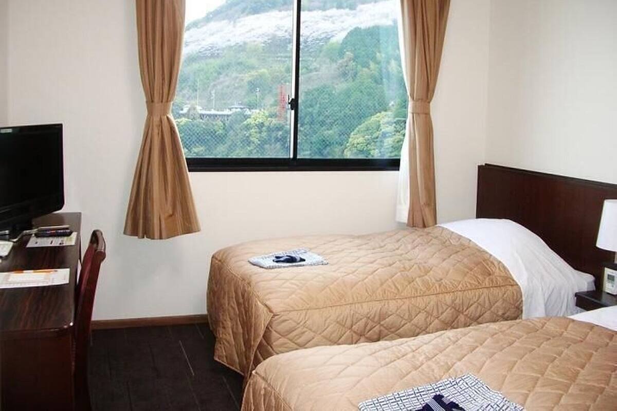Habitación de hotel con dos camas, televisión, escritorio y ventana con cortinas.