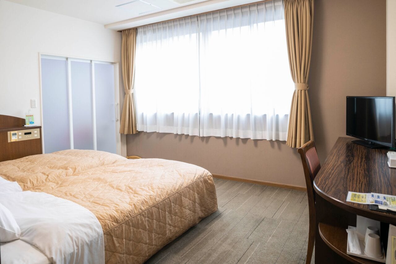 Een hotelkamer met een bed, een bureau, een televisietoestel en een raam met gordijnen.