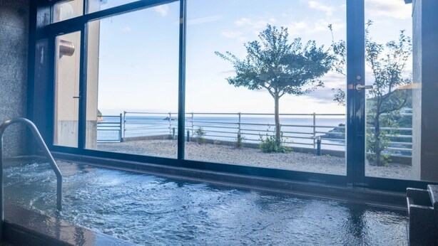 Vista desde una ventana, con una piscina al frente y una playa con vallas y árboles al fondo.