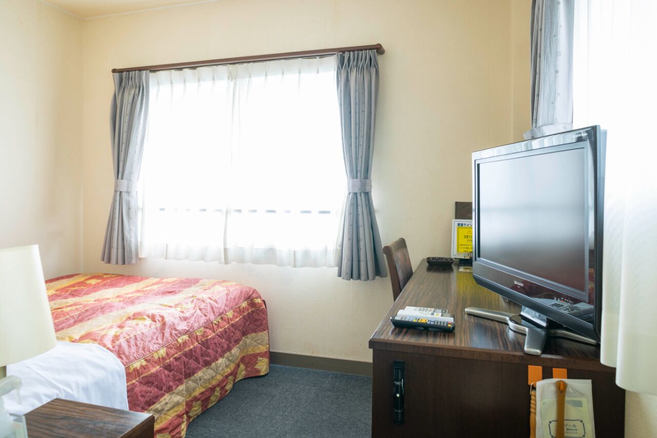 A hotel room with a bed, a desk with a television, and a window with curtains.