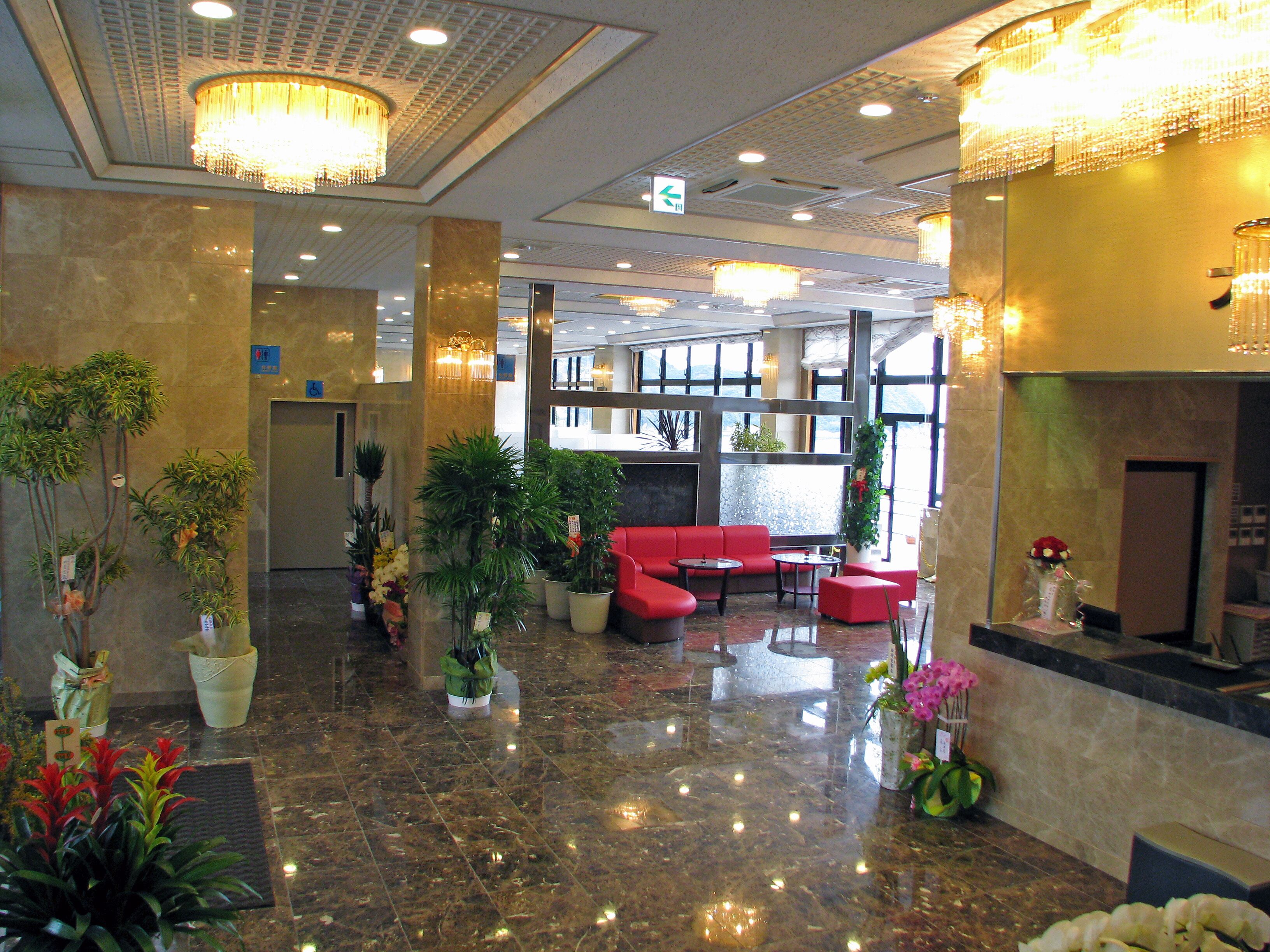 Un hall con un sofá rojo, plantas en macetas y un candelabro.