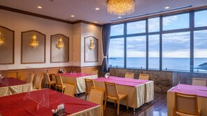 Un restaurante con mesas dispuestas para comer, un amplio ventanal con vistas al mar y apliques decorativos en la pared.