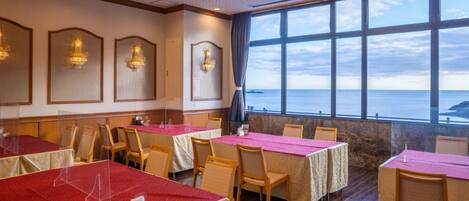 Un restaurante con mesas dispuestas para comer, un amplio ventanal con vistas al mar y apliques decorativos en la pared.