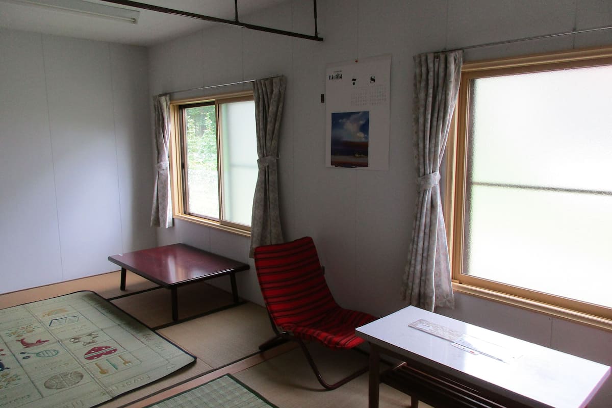 Une pièce comprenant un bureau, une chaise et une fenêtre avec des rideaux. Il y a un calendrier accroché au mur et un tapis sur le sol.