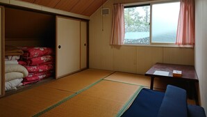 A room with tatami flooring, a bed with red bedding, a small table with a chair, and a window with curtains. - Fresh-Air-Inn (Teshikaga)