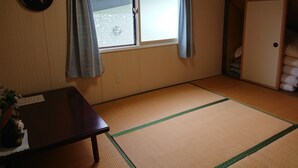 A room with tatami flooring, a sliding door, a table, and a hanging sign. - Fresh-Air-Inn (Teshikaga)