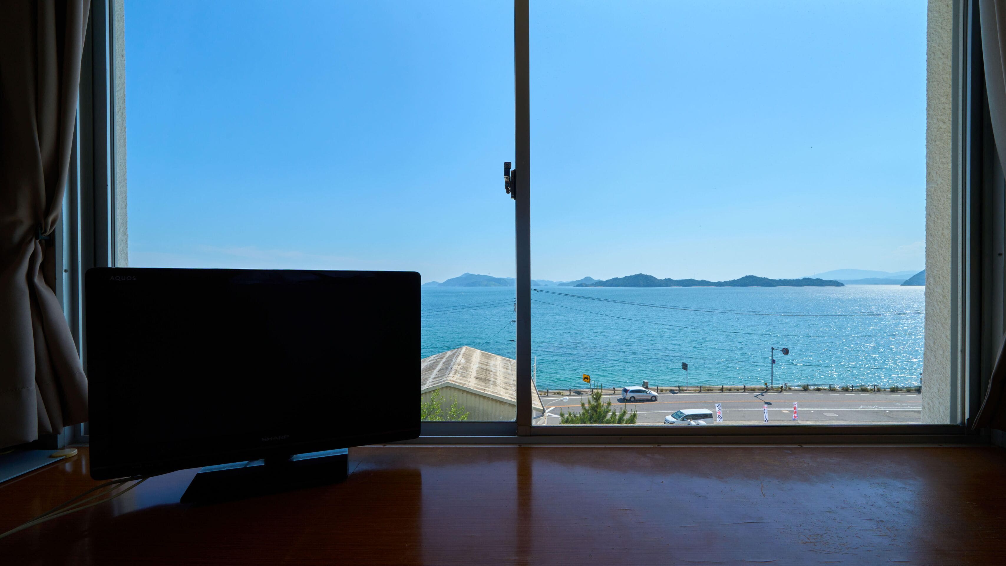 A room with a large window offering a view of the sea and distant mountains.