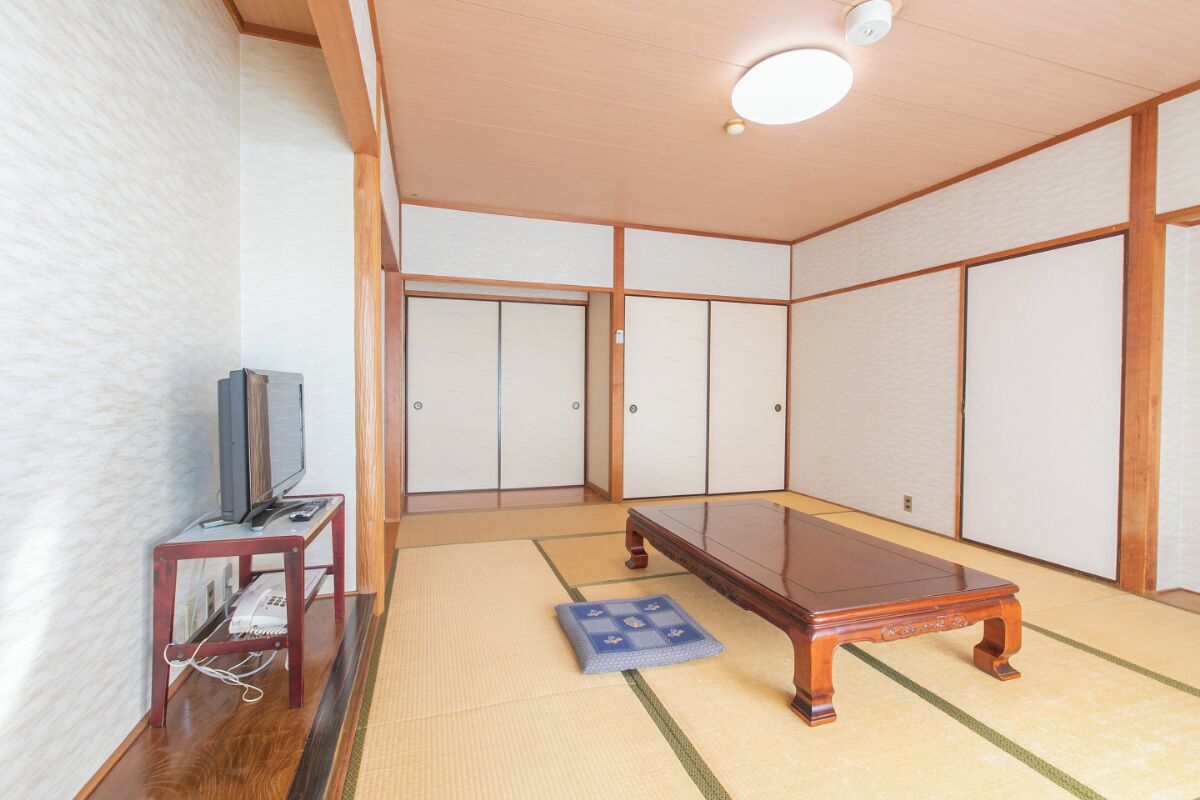 A tatami mat room with a wooden table, a television on a small stand, and sliding doors.