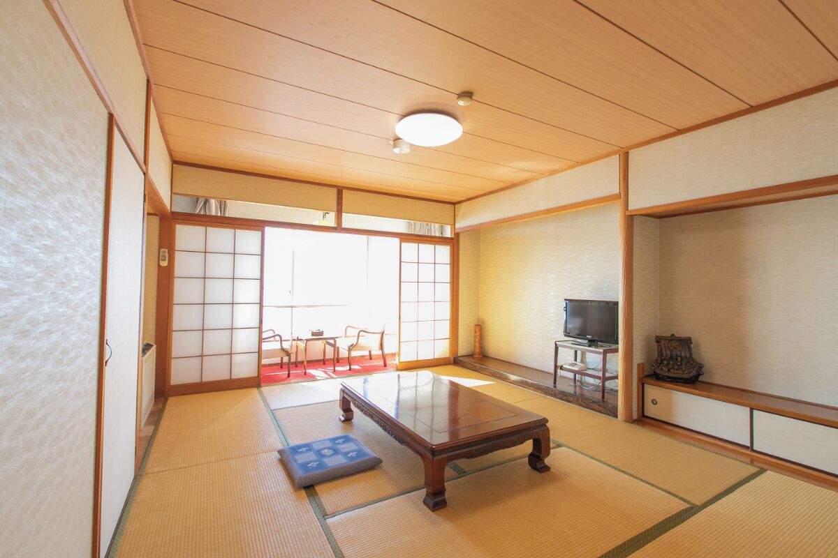 Une pièce de style japonais traditionnel, avec un sol recouvert de tatamis, une basse table en bois, un téléviseur et des portes coulissantes.