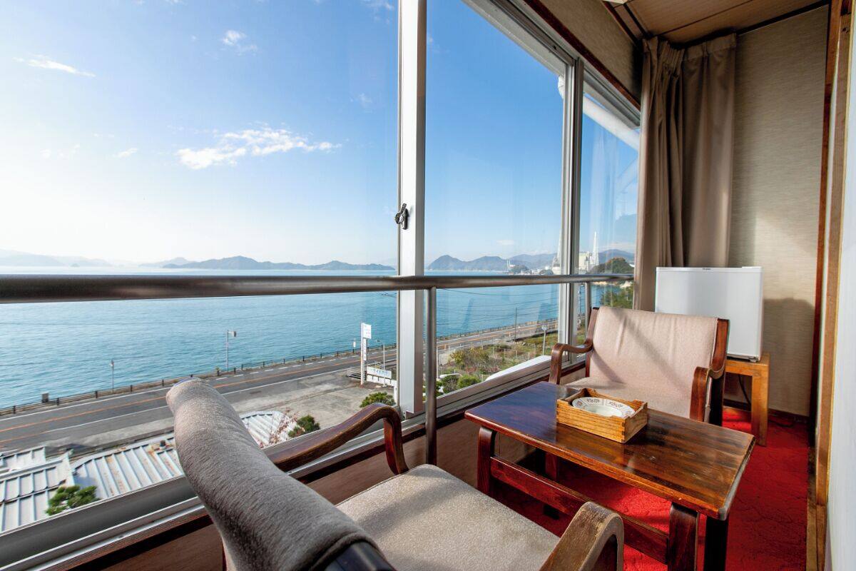 Un balcon avec vue sur la mer et les montagnes, une chaise en bois, une petite table et une lampe.