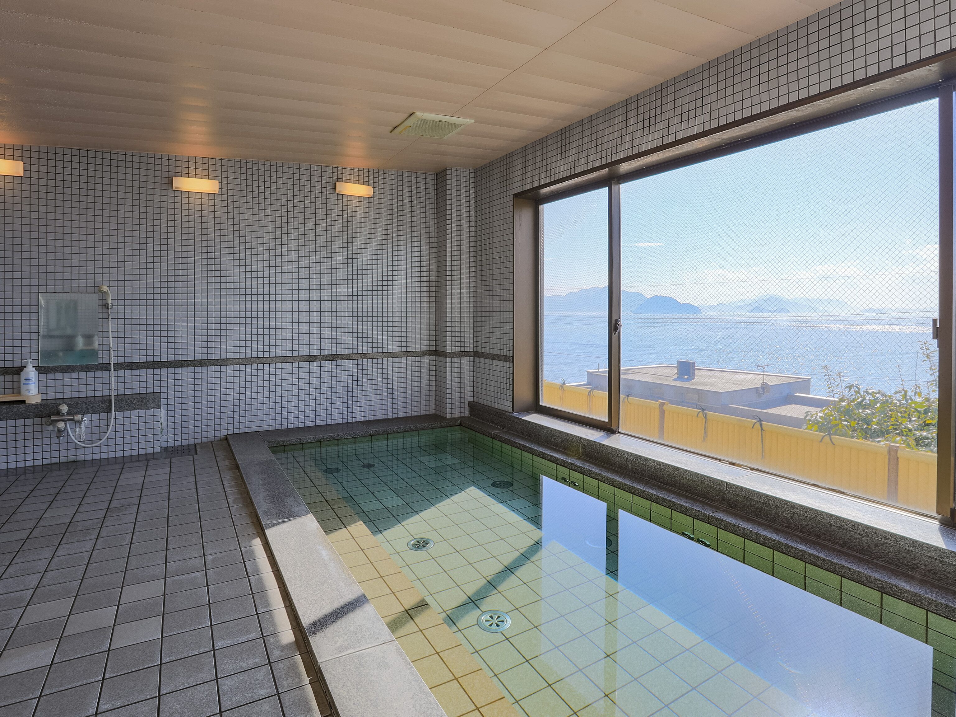 Piscina interior moderna con un amplio ventanal que ofrece vistas al mar y montañas distantes.