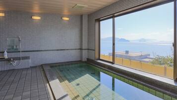 Piscina interior moderna con un amplio ventanal que ofrece vistas al mar y montañas distantes.