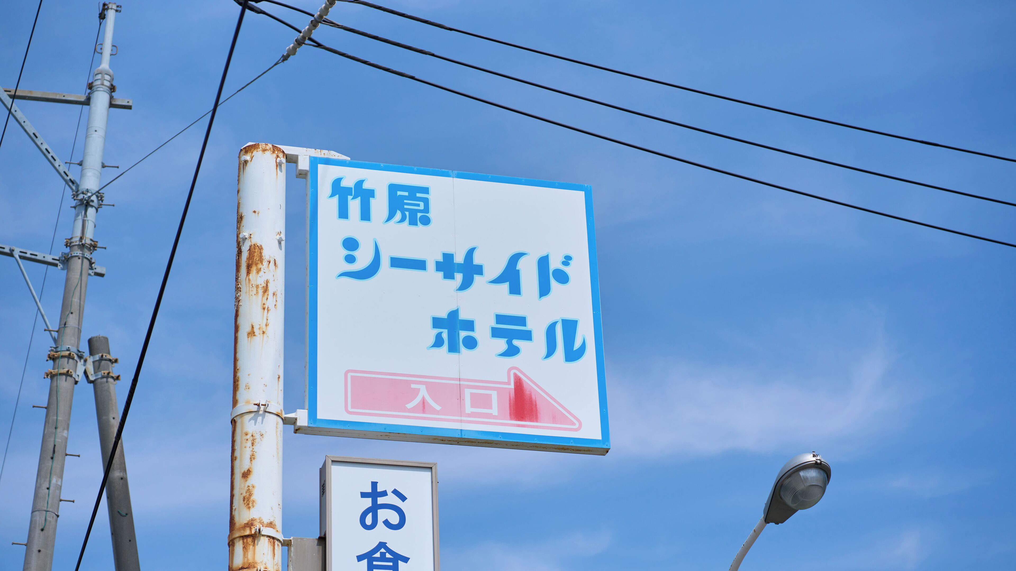 Una señal con texto en japonés y una flecha roja que apunta a la derecha, indicando una dirección o lugar.