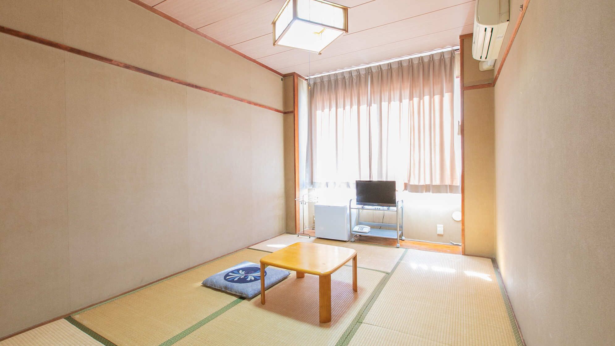 A traditional Japanese room with tatami flooring, a low wooden table, a futon, and a television in the background.
