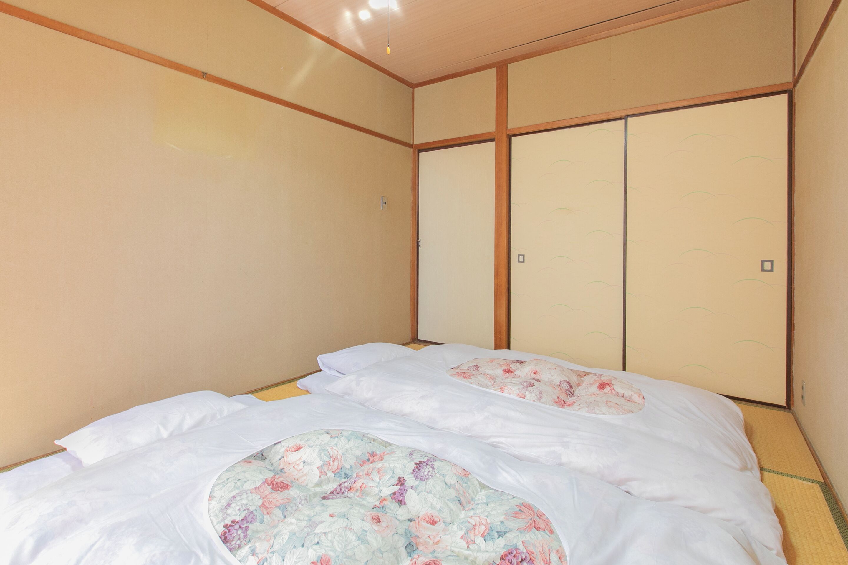 A traditional Japanese room with tatami flooring, a low bed with white bedding and floral-patterned pillows, and sliding shoji doors.