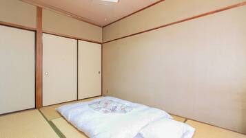 Um quarto japonês tradicional com tatames, futon, portas deslizantes e luminária no teto.