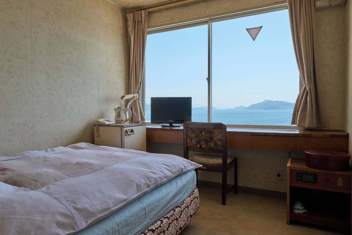 Une chambre d’hôtel avec un lit, un bureau équipé d’un ordinateur, une chaise et une vue sur la mer.