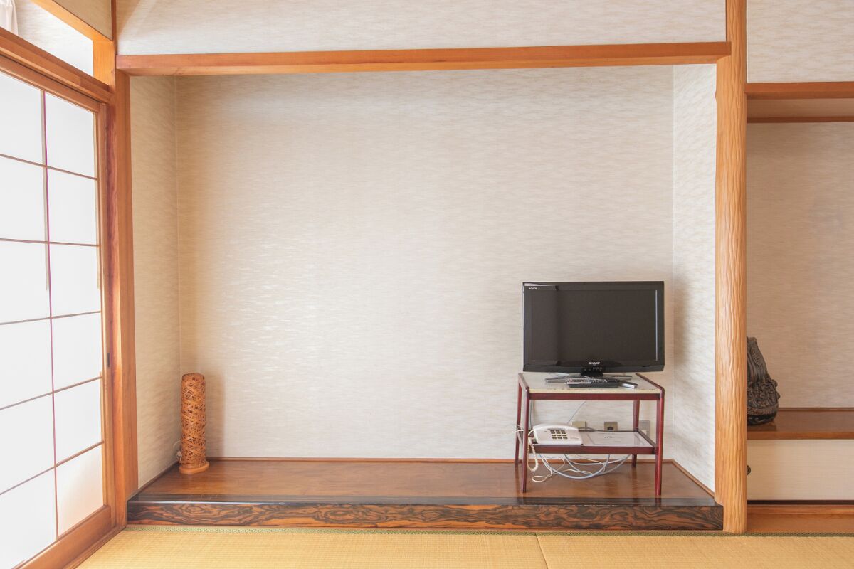Una habitación tradicional japonesa con suelo de tatami, un televisor sobre un mueble bajo y una puerta corredera shoji.