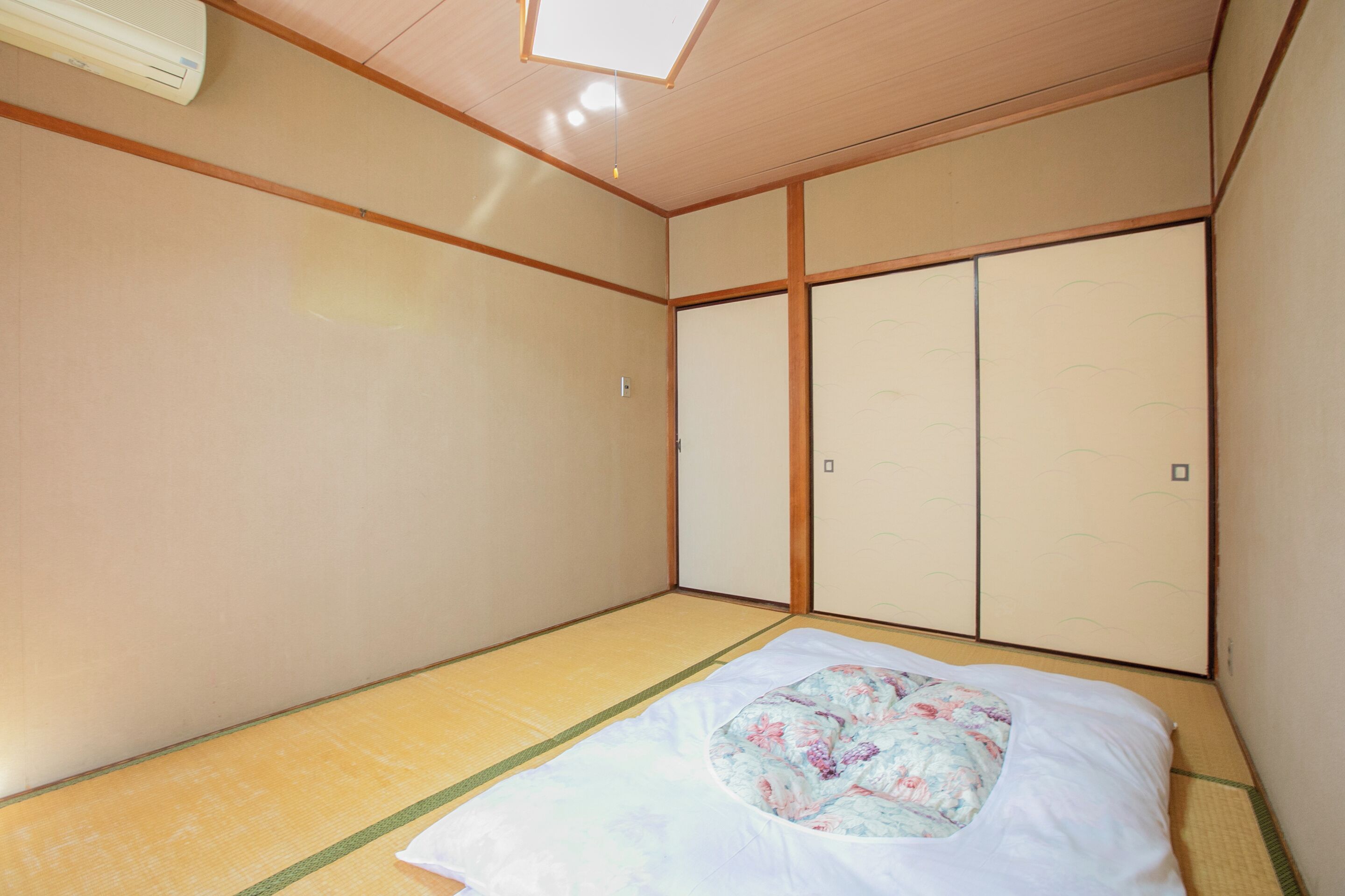 Ein traditioneller japanischer Raum mit Tatami-Bodenbelag, Futon-Bett, Schiebetüren und einem Deckenventilator.