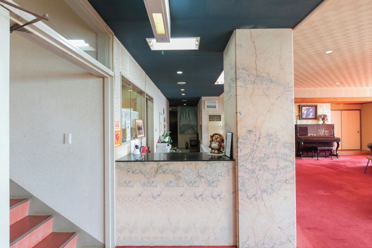 A hotel lobby with a marble reception desk, a staircase, and a piano in the background.