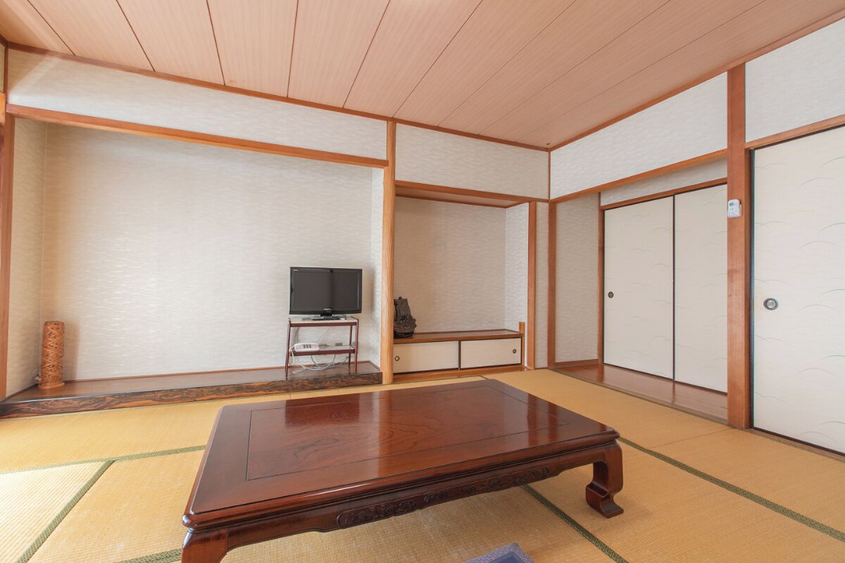A traditional Japanese room with tatami flooring, a wooden table, a television on a low stand, and sliding doors.